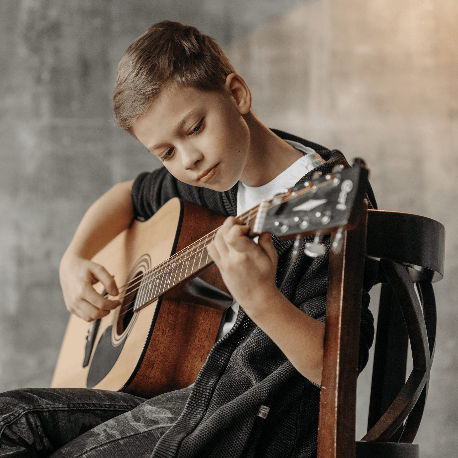 Un petit garçon joue de la guitare, assis sur une chaise.